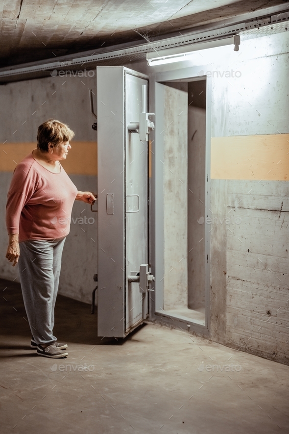 Senior woman entering nuclear fallout shelter built under the house to hide from nuclear explosion