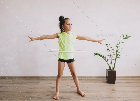 Cute teenage girl doing gymnastics at home. The girl spins the hoop.