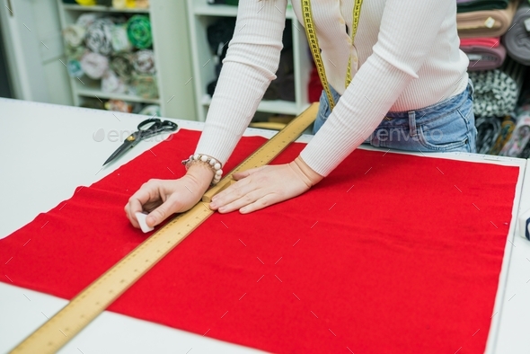Woman measuring fabric on work table in textile store. Seller working with tissue in drapery shop.