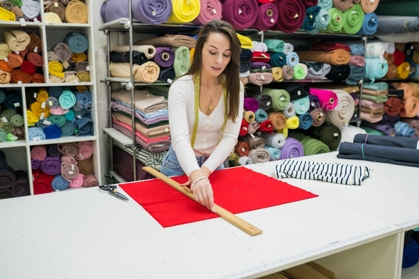 Woman measuring fabric on work table in textile store. Seller working with tissue in drapery shop.