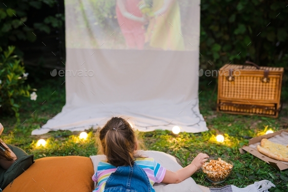girl lying on the grass watching movie on projector in the backyard