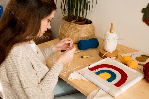 Young woman making stitchs through holes in the monks cloth fabric on pattern in workshop.