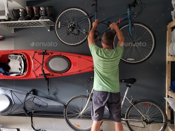 Man reaching up for a bike in neat and organized garage with shelves and racks, efficient storage