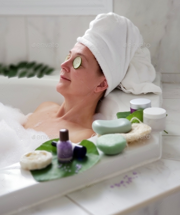 Woman is relaxing in foamy bathtub and having some facial skin treatments to fight aging