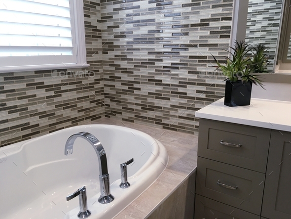 New bathtub installed at the window, mosaic tiles decorate wall, stainless steel faucet