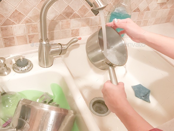 Woman’s hands washing pots and pans in kitchen sink