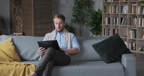 Thoughtful Young Businessman Freelancer Typing on Laptop Sitting Sofa at Hom alt