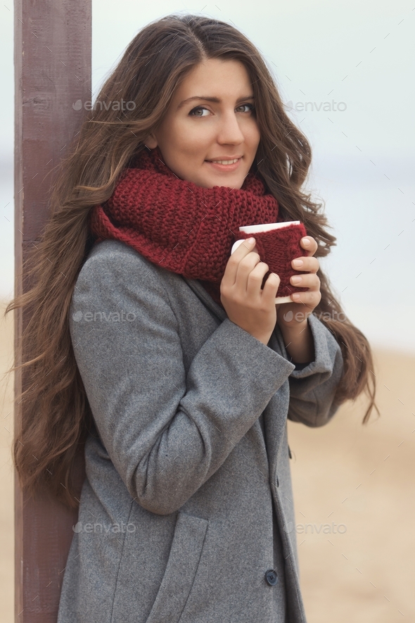 A girl enjoys the sound of the ocean shore and holds a cup of aromatic coffee in her hands
