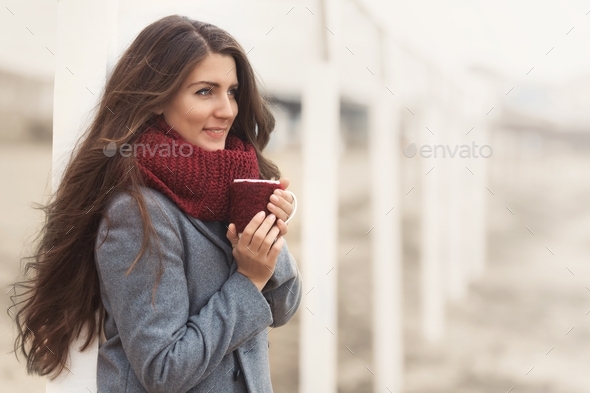 A girl enjoys the sound of the ocean shore and holds a cup of aromatic coffee in her hands