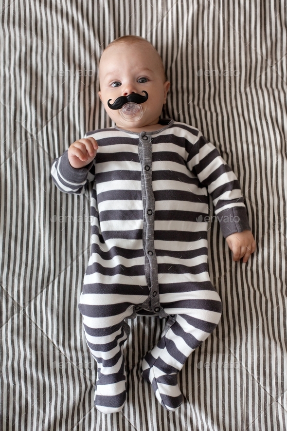 Cute mini man baby boy 6 months old in funny striped pajamas and