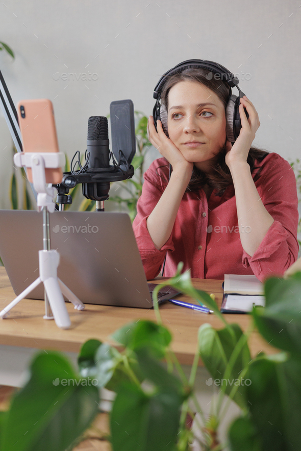 woman in a home office records podcast audio content with a microphone and headphones and a labrador