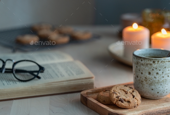 Reading book on cozy winter evening with candles, tea and cookies.