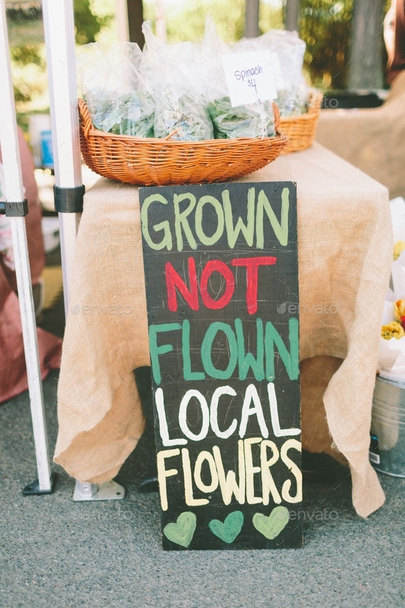 A sign at a farmers market saying ‘grown not flown’ supporting local businesses.
