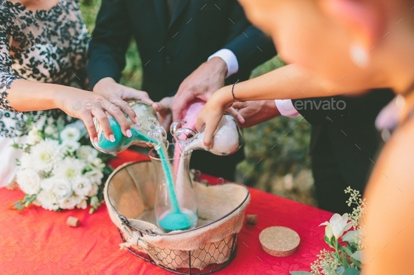 Hands pouring coloured sand into a glass jar at a sand pouring ceremony ...