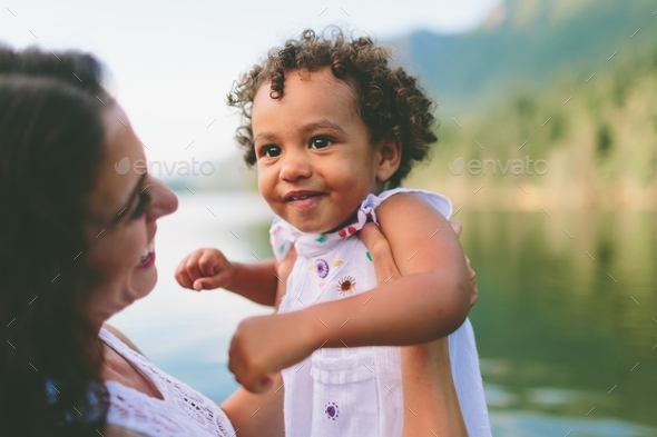 A mixed race little girl being picked up by her mother at the lake.