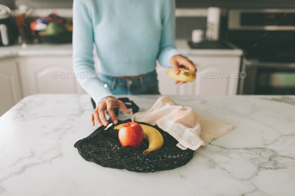 A woman pulling groceries out of a sustainable, eco-friendly reusable bag while in the kitchen. - Stock Photo - Images