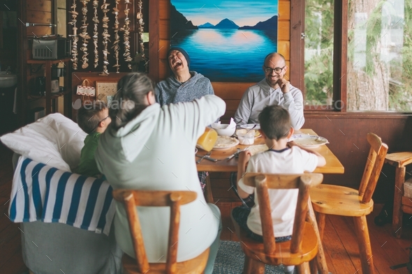 A family sitting together around a dining table in a cabin having a meal. - Stock Photo - Images