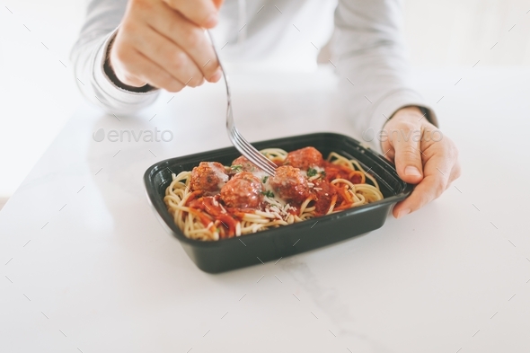 Hands eating a take out lunch of spaghetti and meatballs on a white counter. - Stock Photo - Images