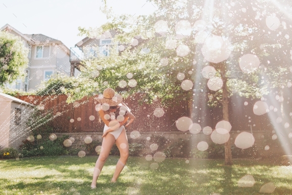 A woman holding a little boy while running through the sprinkler on a sunny summer day.  - Stock Photo - Images