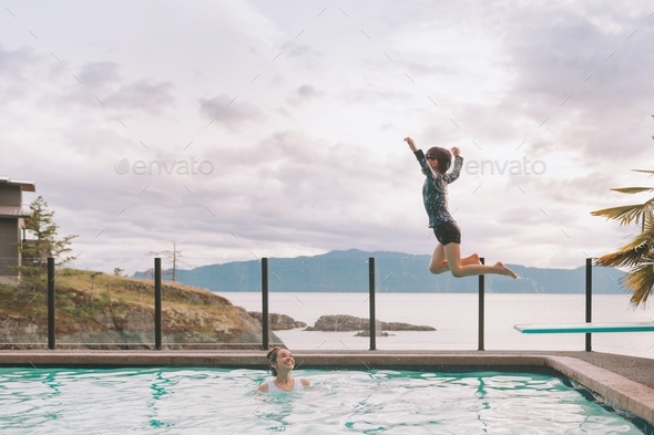 A little boy jumping off of a diving board into a pool by the ocean. - Stock Photo - Images