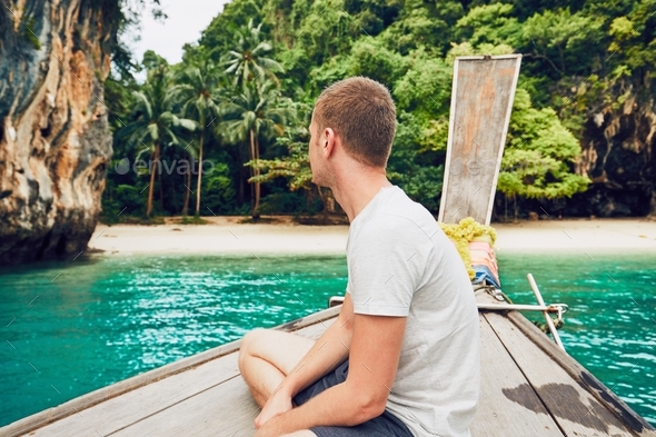 Tourist (young man) on the traditional long tail boat against lagoon - Stock Photo - Images