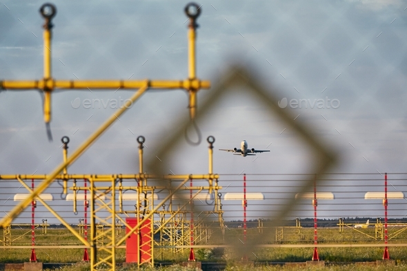 Traffic at the airport. Airplane during take off over landing lights (view through the fence).