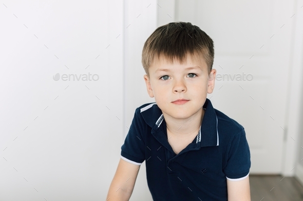 Portrait of cute boy in navy blue T-shirt in bedroom at home.
