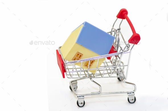 shopping basket with a model of a house on the road with US dollar bills, isolated