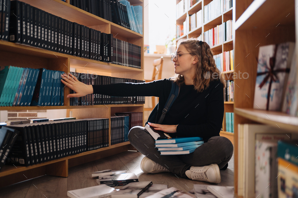 Teenager girl picking a book on a library shelf - Stock Photo - Images