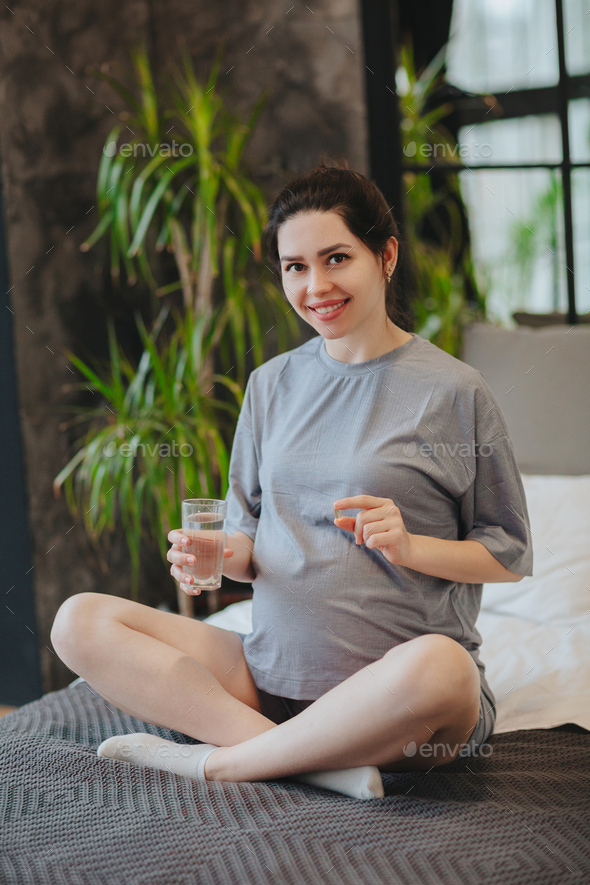 Pregnant woman taking prenatal vitamins during pregnancy, holding water glass and pill in hands