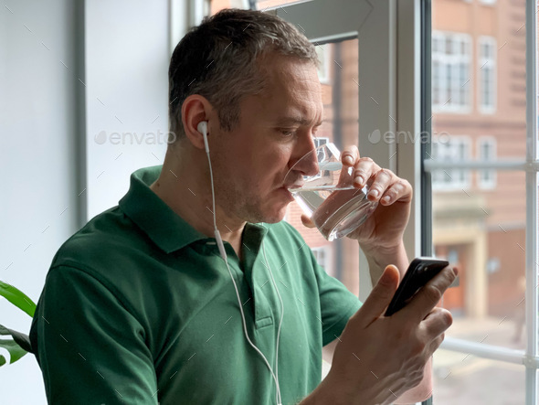 Middle aged thirsty man is drinking water white having video call, hangover. Pure life still water