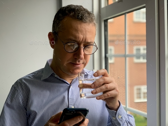 Middle aged thirsty man is drinking water white having video call, hangover. Pure life still water