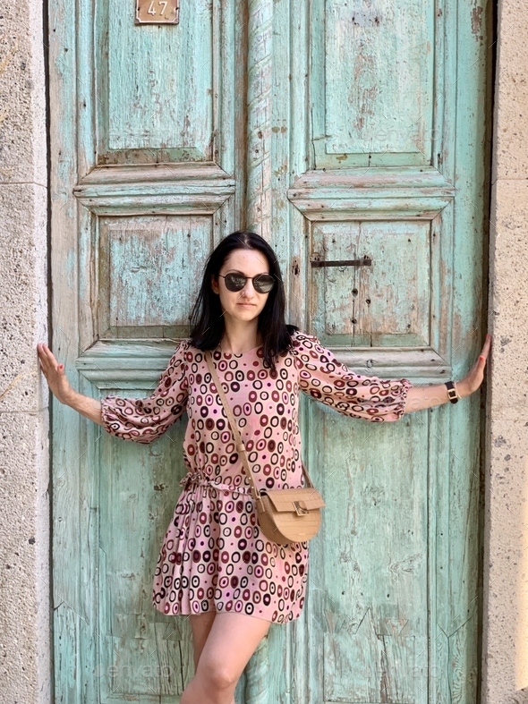 A dark haired girl in silk beige dress with abstract pattern and cross body bag