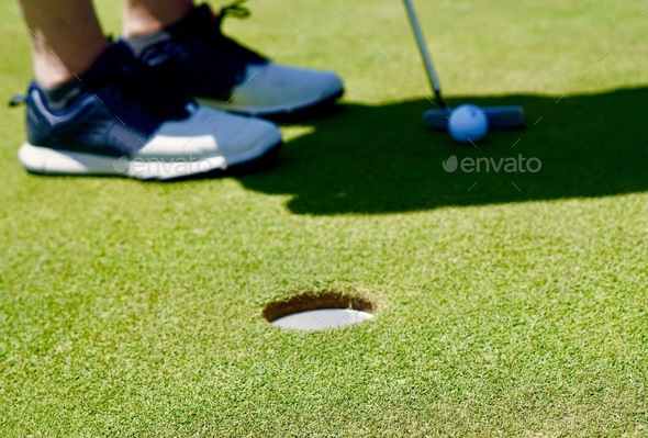 Closeup on the putting green of hole, feet, golf ball and putter golf club