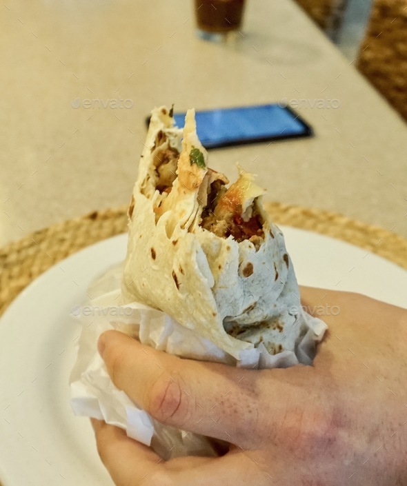 Closeup view of male hand holding a big burrito with a couple of bites missing