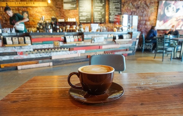 A latte on a table with coffee bar in the background in a coffee shop or third wave coffee roastery