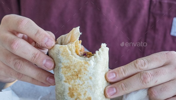 Two hands holding a fish and cactus burrito with one big bite missing