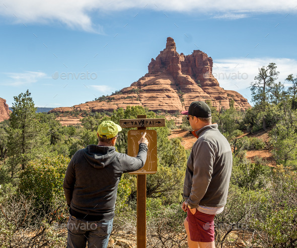 View from behind of two adult males looking at a trail map and red rock formation in the background