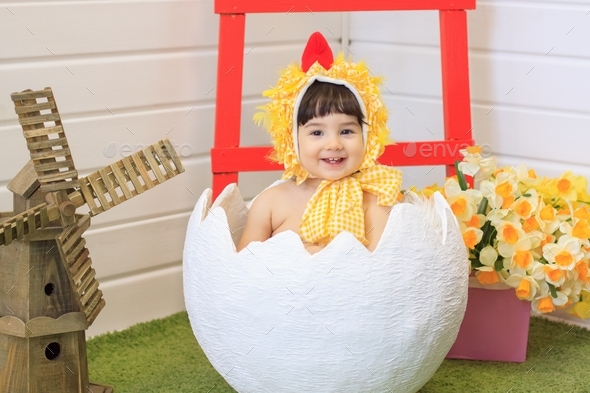 Cute Little baby girl in a yellow chicken costume sits in big egg