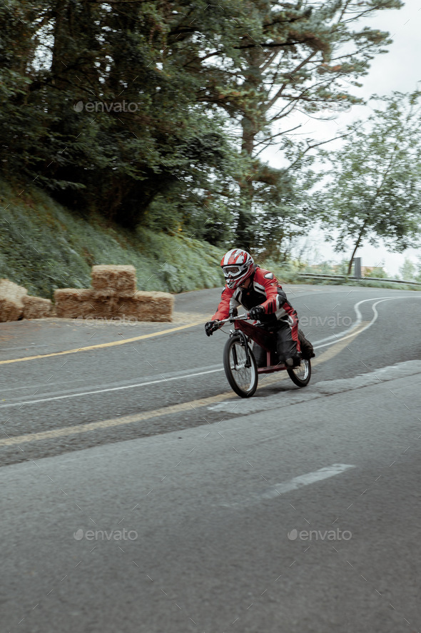A man slides at high speed down a road in little bike wearing a helmet and protective suit.