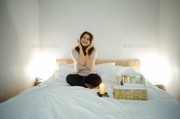 Young smiling woman listing music on bed