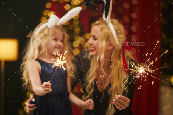 Happy mother and daughter wearing rabbit ears celebrating, holding sparkles, smiling.
