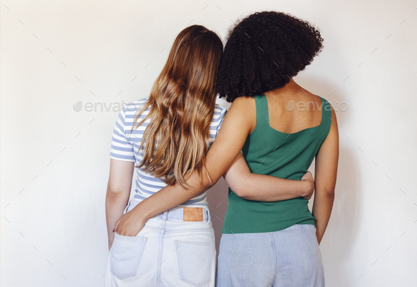 Rear view two teen girls best friends holding hands behind back and hugging while standing in front