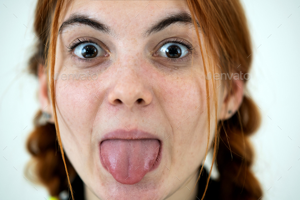 Closeup portrait of a funny redhead teenage girl with childish hairstyle sticking out her tongue