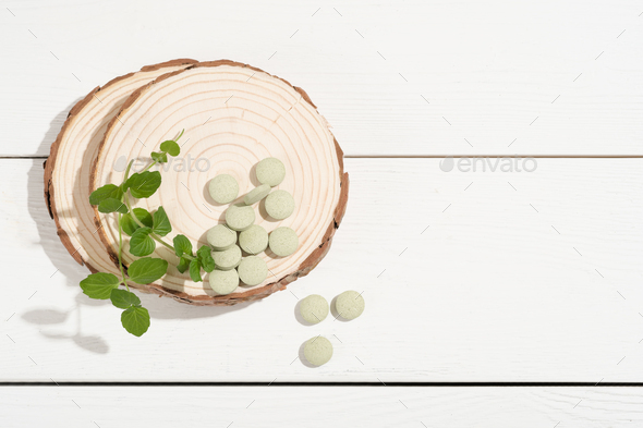 Spirulina green pills on wooden saw cut on a white table. Chlorella tablets. Green detox, . - Stock Photo - Images