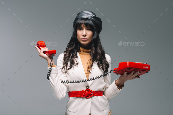 attractive brunette woman in white suit with red landline phone isolated on gray