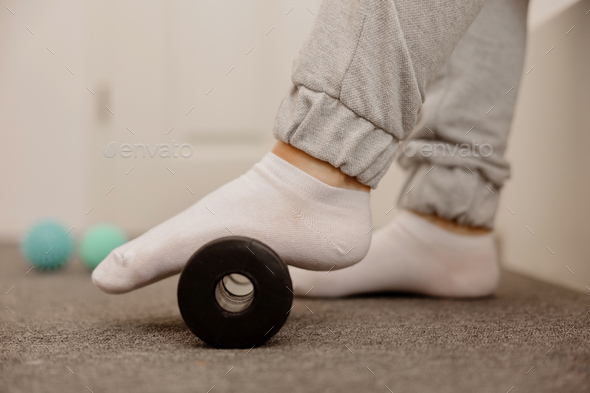 Woman doing flatfoot correction gymnastic exercise using massage roller.
