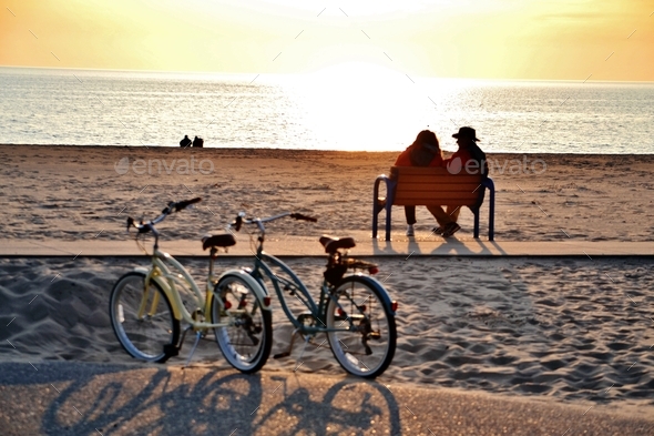 Couple sitting on a bench at the beach watching the sunset. - Stock Photo - Images