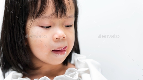 Cute child is licking the cream cake that follows her lips luscious.