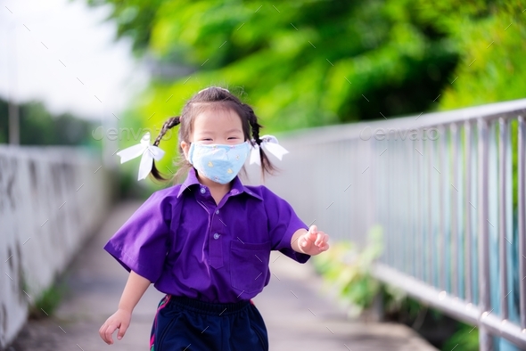 Student wearing blue cloth face mask runs on road. Children wear purple sports uniforms of school.